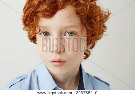 Close up portrait of funny little kid with orange hair and freckles. Boy looking in camera with relaxed and calm face expression