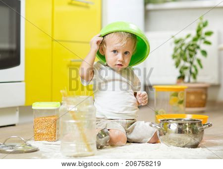 Child toddler boy sitting on the kitchen floor and playing with flour.