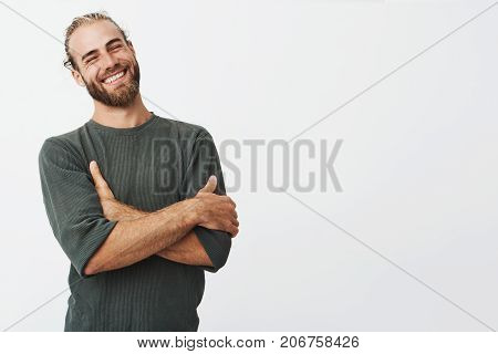 Attractive swedish man with stylish hair and beard laughs at funny story from friend with crossed hands and closed eyes