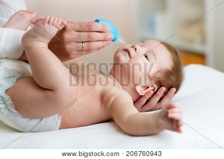 Mother or doctor cleans baby's nose with blower while infant tot is lying and smiling.