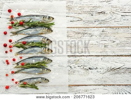 Fresh raw fish Baltic herring on white wooden table with fresh herbs and cowberry. View from above. Copyspace for text.