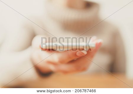 Female holding smartphone while sitting at wooden table, selective focus, close up.