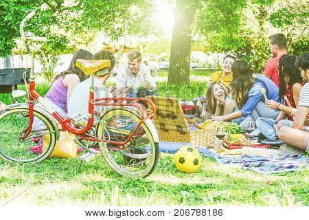 Group of a lot of people having a tasty picnic eating and drinking red wine in a park outdoor - Happy friends celebrating a sunny day sharing drinks and foods - Traditional meal merged with nature
