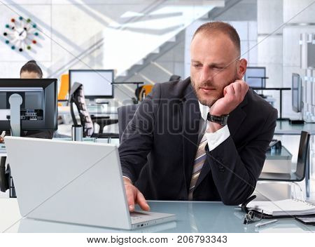 Confident caucasian stock broker working at bright financial business office desk with laptop computer. Determined, suit.