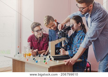 Stem education. Teenagers with teacher making chemical experiment in laboratory with reagents and microscope. Early development concept