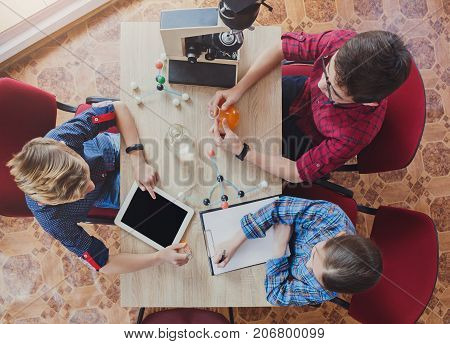 Stem education. Teenagers studying at biology lesson in laboratory, sitting with equipment, using gadget and blank notebook, top view, copy space