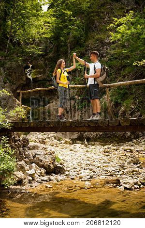 Active Young Cople Hiking On A Wooden Brifge Over Mountain Creek