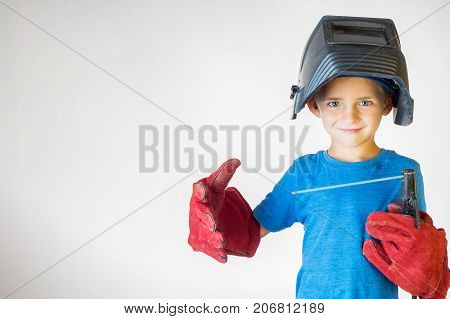 Happy little kid in welder mask and welding equipment. Welding equipment welding mask protective leather gloves welding electrodes. Fun concept. Child dreaming of future profession. Career choice.