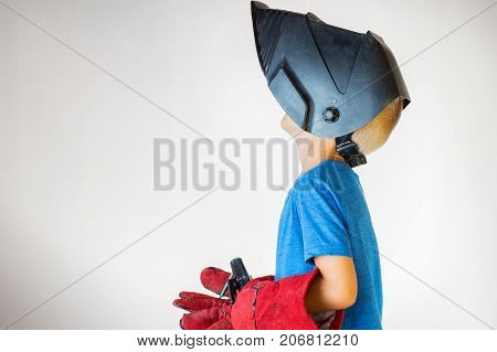 Happy little kid in welder mask and welding equipment. Welding equipment welding mask protective leather gloves welding electrodes. Fun concept. Child dreaming of future profession. Career choice.