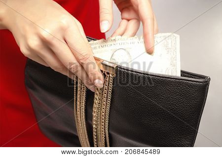 Young woman in red dress with black leather clutch bag in her hands. The girl gets all the money from her purse. Last money.