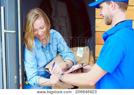 Smiling delivery man in blue uniform delivering parcel box to recipient - courier service concept. Smiling delivery man in blue uniform