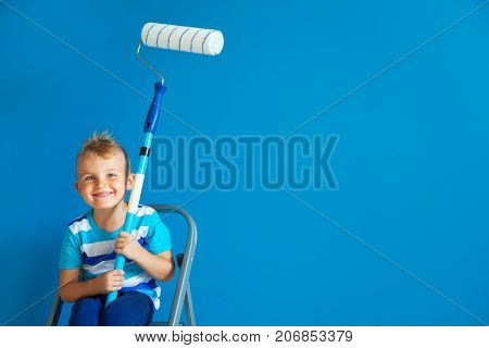 The child paints the blue wall with a roller. The boy holds a large brush for painting. Home repairs.