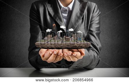 Cropped image of businessman in suit presenting in his hands modern city block with gray wall on background. 3D rendering.