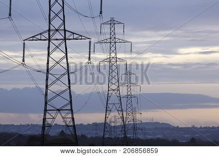 Electrical pylons at sunset leading to a populated area  to provide the necessary power,