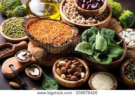 Healthy vegan food assortment. Leguminous, nuts, broccoli, spinach and seeds on dark rusty table.