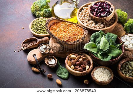 Healthy vegan food assortment. Leguminous, nuts, broccoli, spinach, oil  and seeds on dark rusty table with copy space.