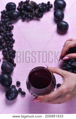 composition of wine, grape and plums on a pink background
