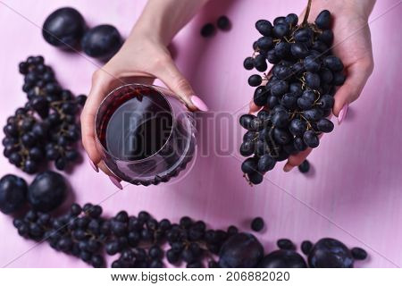 composition of wine, grape and plums on a pink background