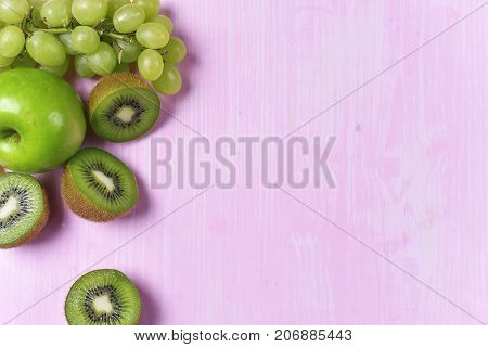 composition of kiwi, grape and apple on a pink background
