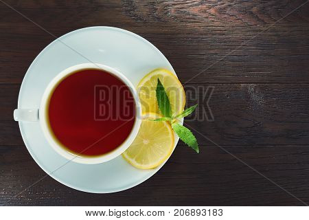 White porcelain cup of tea with cinnamon sticks, lemon, mint leaves and tea strainer on wooden rustic table.