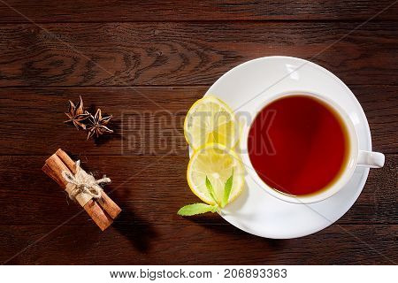 White porcelain cup of tea with cinnamon sticks, lemon, mint leaves and tea strainer on wooden rustic table.