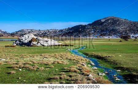 Amazing panorama of Omalos plateau with lake, snowy mountains, grass, cloudy blue sky, Lasithi, Crete