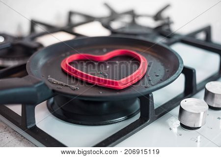 A man cooks an omelette in a beautiful kitchen on a gas cooktop in a heart shaped form. Conceptual photo