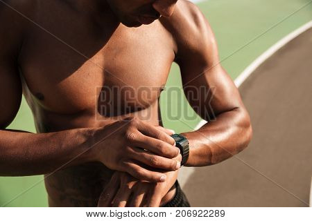 Cropped photo of half naked afro american musculary sports man checking time on wristwatch after workout