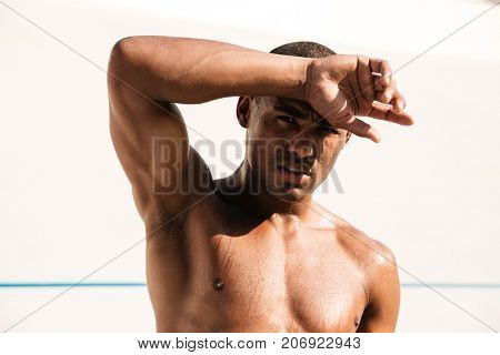 Tired wet athletic african man wiping sweat with his hand, stadium outdoor