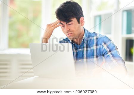 Tired designer touching his forehead in front of laptop