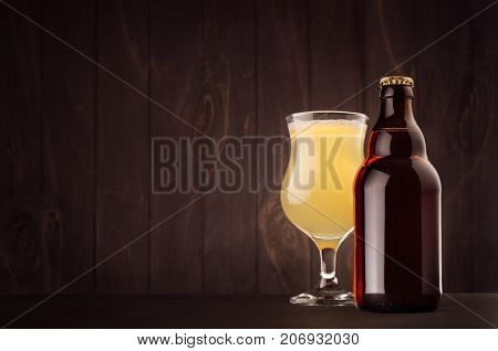 Brown beer bottle belgian steinie and glass tulip with muddy weizen on dark wood board copy space mock up. Template for advertising design branding identity.