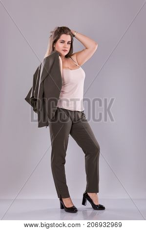Portrait of a plus size female model posing in broun costume over grey background. Beautiful woman with curvy figure.