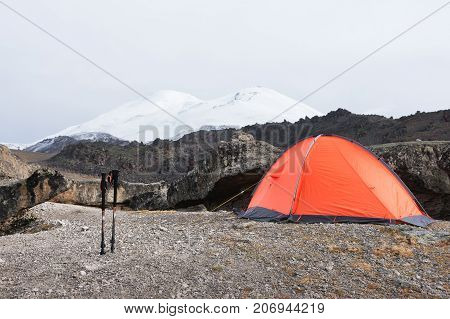Trekking mountain sticks stand near a stone near the orange trekking tent on the deserted stone slopes of the elbrus between the rocks called the Stone mushrooms.