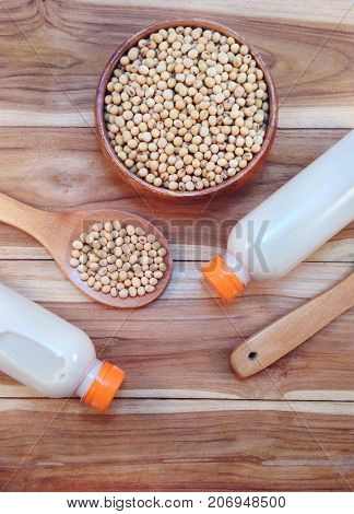 Soy milk in bottle and soy beans with wooden ladle on wooden background