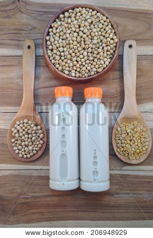 Soy milk in bottle and soy beans with wooden ladle on wooden background