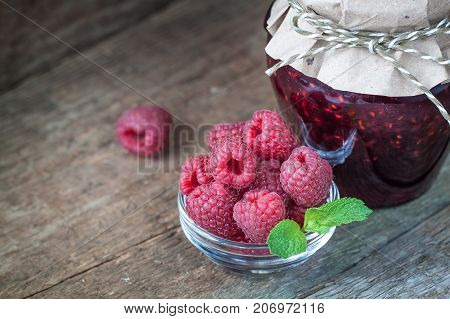Raspberry jam with fresh raspberries on the old wooden background