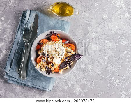 Tasty italian fusilli pasta with cherry, mozarella or buratta cheese and fresh basil. Dish with pasta on gray concrete background. Top view. Copy space. Healthy food concept and recipe idea.
