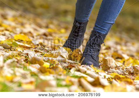 woman feet boots walking on fall leaves outdoor with autumn season nature on background