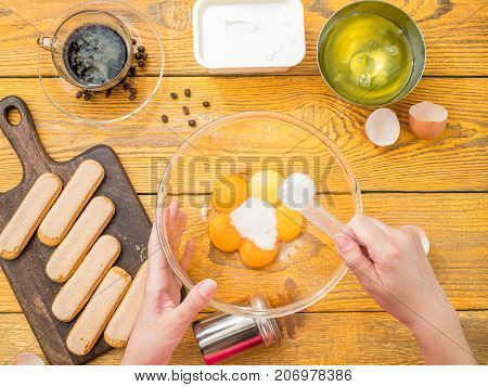 Image on top of table with savoyardi cookies, hands with cup of eggs, coffee