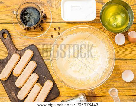 Picture of wooden table with savoyardi biscuits, coffee, cup, cream cheese.