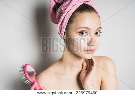 cute girl with a pink towel on the glove holds a multicolored comb on a white background