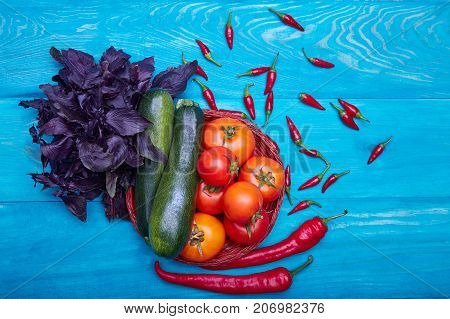 Beautiful composition of harvest autumn vegetables: red tomatoes, chili peppers, green zucchinis and purble basil on a blue wooden background.