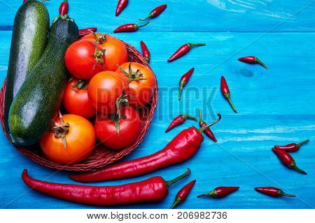 Beautiful composition of harvest autumn vegetable ingredients: red tomatoes, chili peppers, green zucchinis on a blue wooden background.