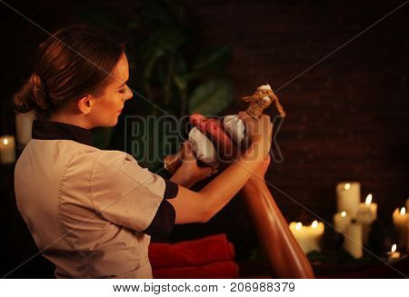 Feet massage with Thai reflexology. Cropped shot of foot reflexology. Body part of female hand and leg on candels background. Masseuse in foreground. Rest in an elite beauty salon.