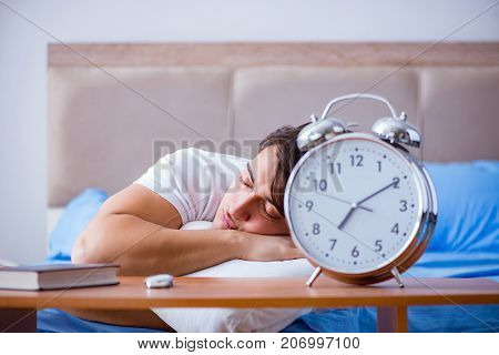 Man in bed frustrated suffering from insomnia with an alarm cloc