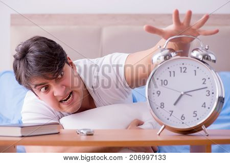 Man in bed frustrated suffering from insomnia with an alarm cloc