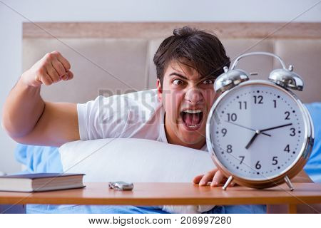 Man in bed frustrated suffering from insomnia with an alarm cloc
