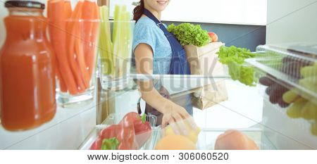 Portrait of female standing near open fridge full of healthy food, vegetables and fruits. Portrait of female