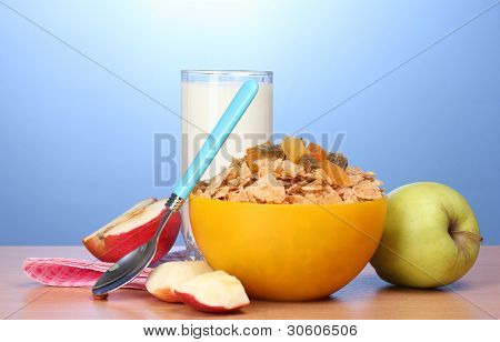 leckere Cornflakes in gelbe Schale, Äpfel und Glas Milch auf Holztisch auf blauem Hintergrund