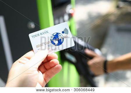 Male Hand Hold White Plastic Credit Card Aganist Gasoline Station. Wireless Payment Terminal Concept